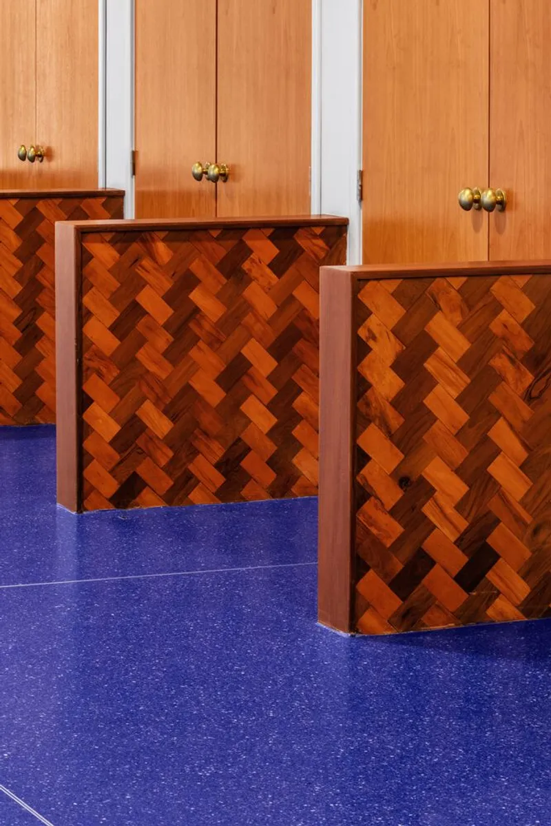 Herringbone wood veneer reception desks with brass hardware against blue carpet and vertical wood paneling