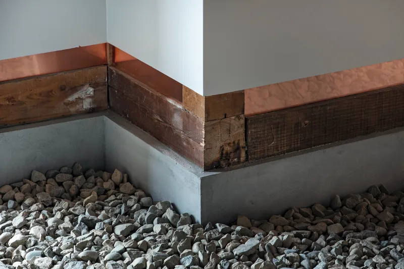 Corner detail of reclaimed timber beam with copper cap above concrete base filled with river stones