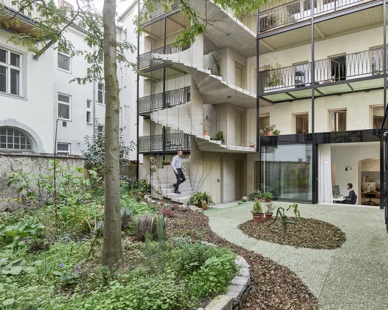 Courtyard view of the terraced rear facade with planted balconies and mesh railings adjoining a planted garden