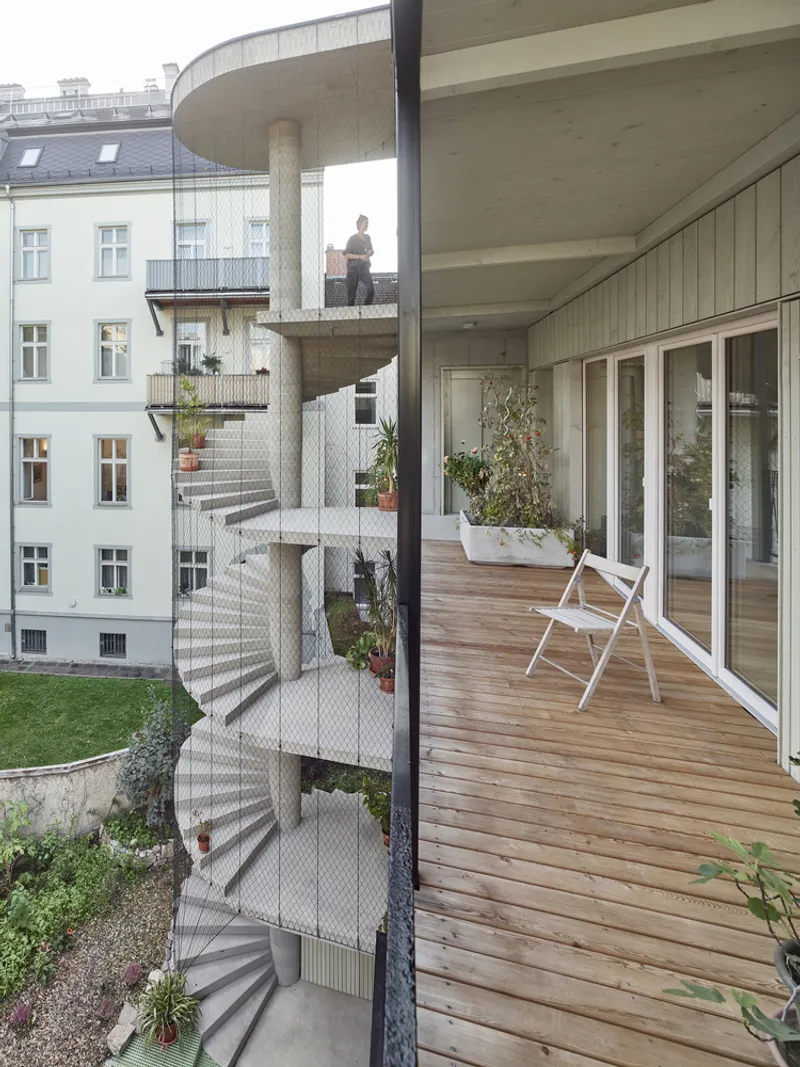Timber balcony deck with white folding chair looking out toward the spiraling concrete stair tower clad in mesh
