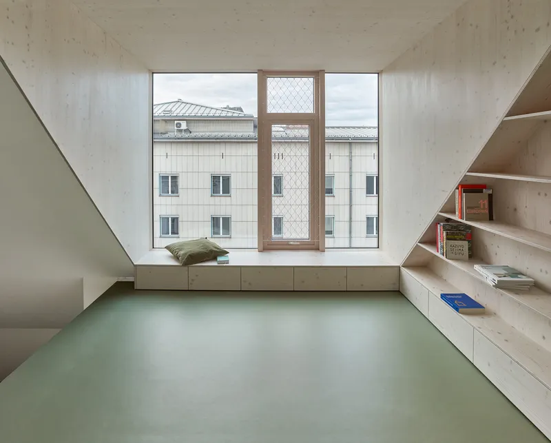 Interior room with pale green floor, built-in timber shelves and window seat overlooking neighboring rooftops