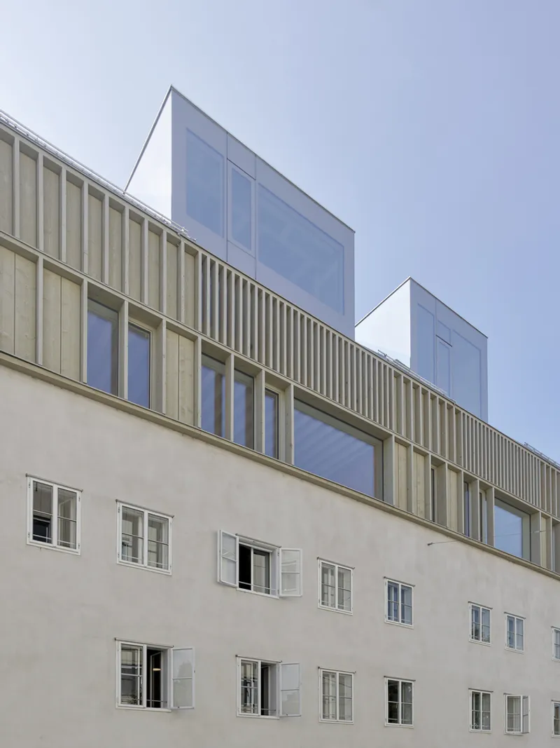 Street facade showing ribbed timber cladding atop a stucco base with paired glass volumes rising above