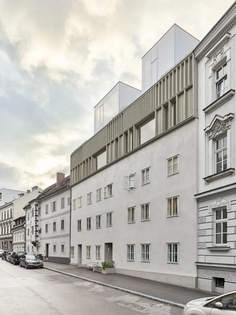 Street elevation of the timber-clad rooftop addition atop a historic stucco facade under overcast skies