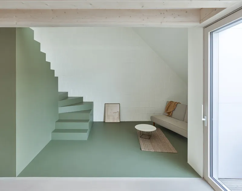 Cantilevered sage-green staircase rising against a white wall beneath a timber ceiling