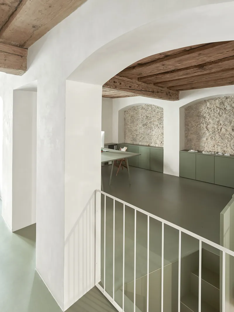 Split-level interior with exposed timber beams and olive-green cabinetry beneath textured stone arches