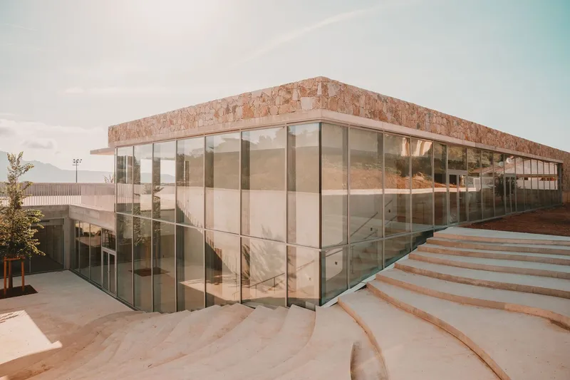 Corner view of the glazed facade and curved stone steps in afternoon light