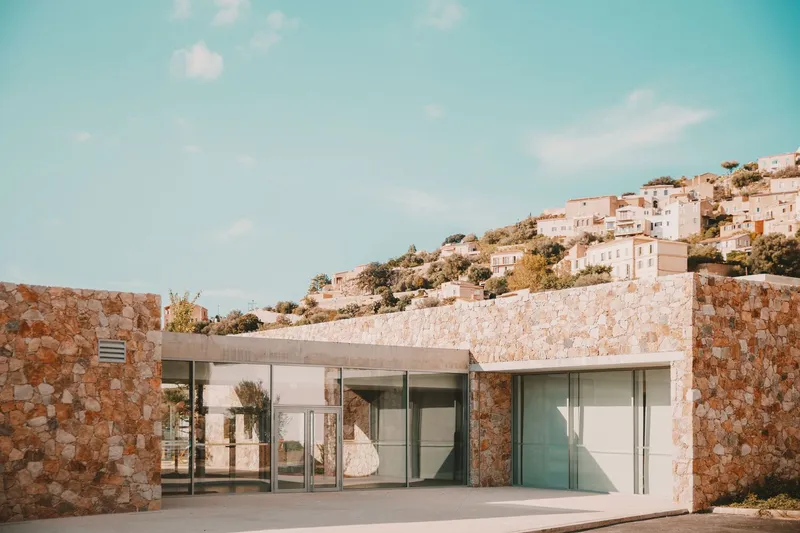 Entry facade with floor-to-ceiling glass framed by rough-cut stone walls under a clear sky
