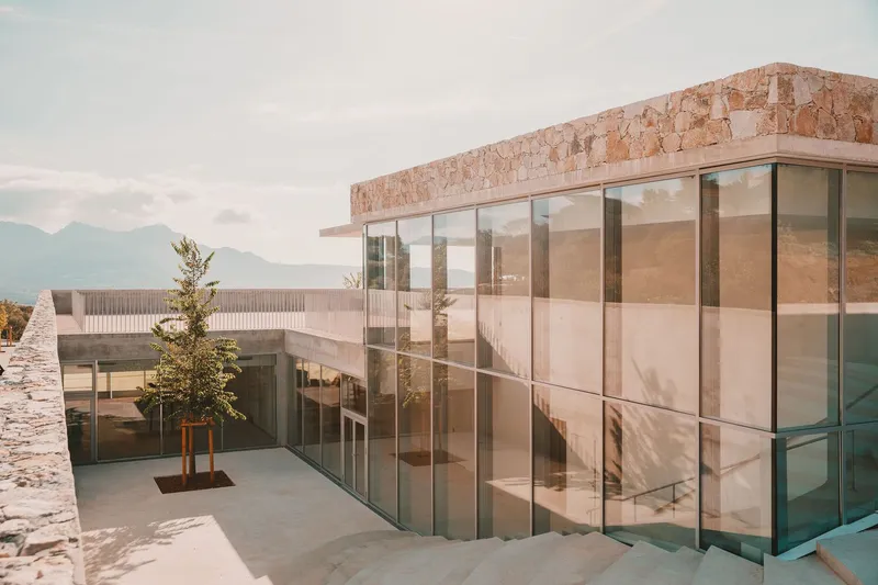 Sunken courtyard with floor-to-ceiling glass walls and a stone parapet against distant mountains