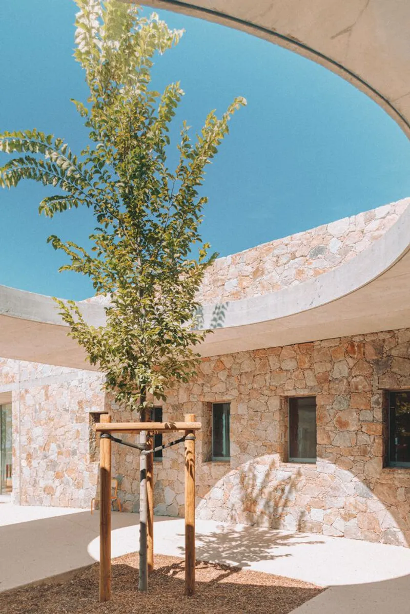Circular roof opening framing sky above courtyard with planted tree and stone walls