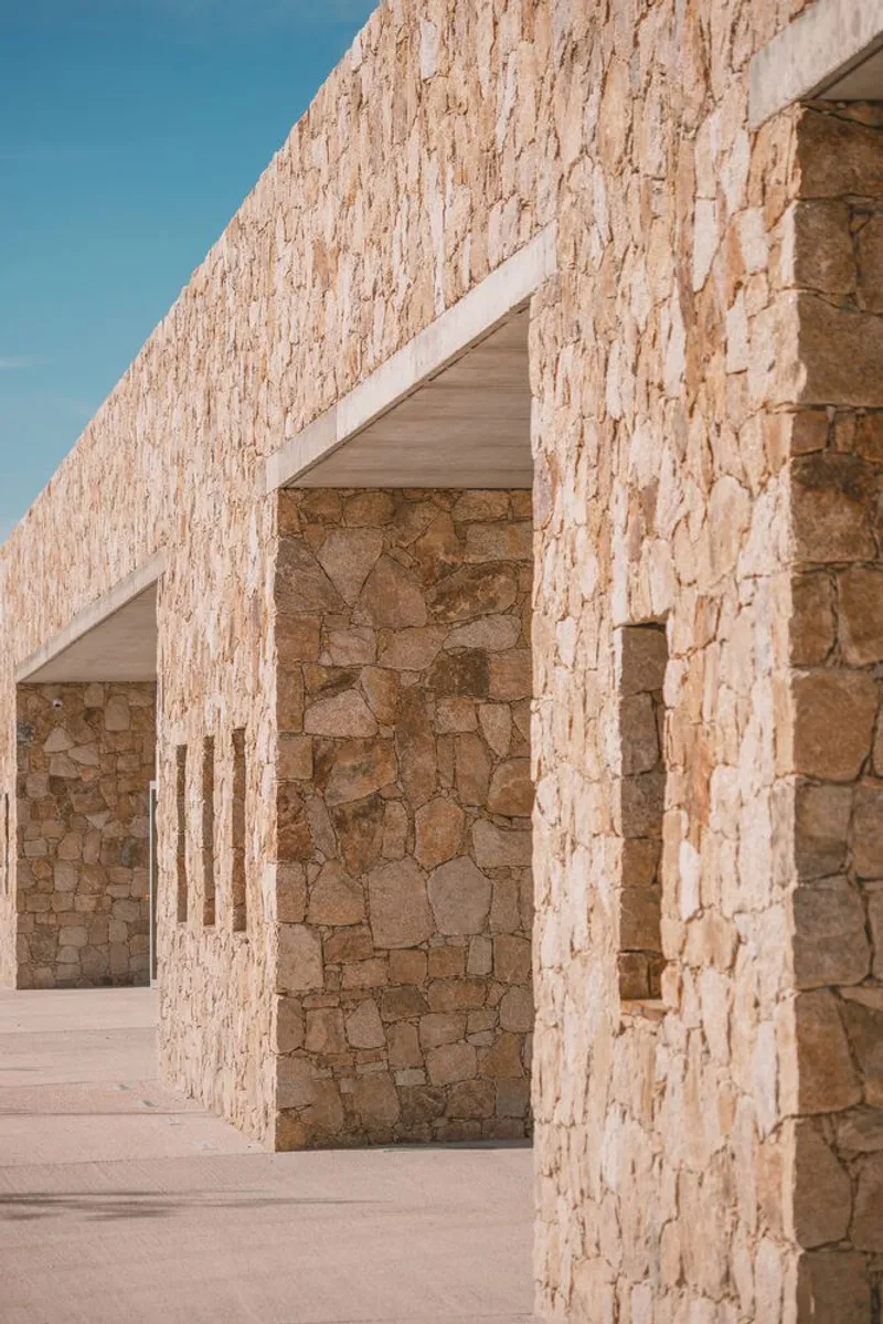 Colonnade with rough stone piers and pitched stone parapet against a clear blue sky