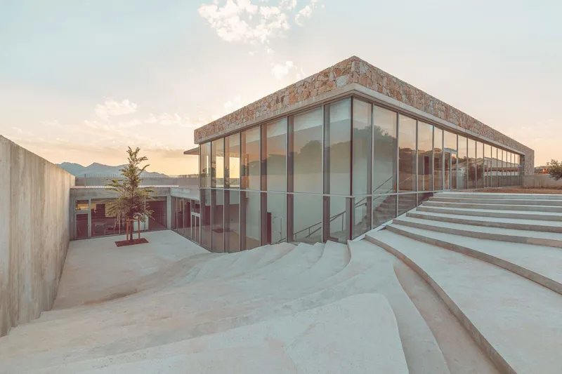 Glass pavilion with weathered copper roof adjacent to curving stone amphitheater steps at dusk
