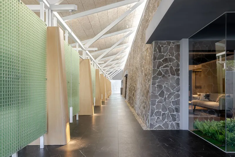 Interior corridor with green textured glass partition, stone wall cladding, and white triangular ceiling trusses