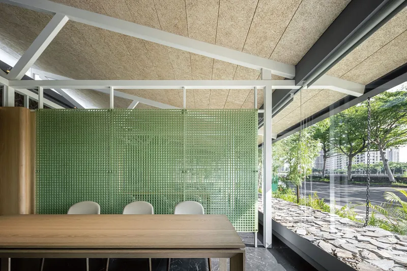 Meeting table with white chairs against green textured glass screen under exposed ceiling panels and white beams