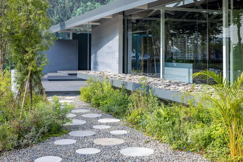 Circular stepping stones through gravel leading to glass-walled entrance with reflecting pool and planted palms