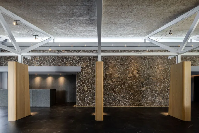 Lobby space with cylindrical timber columns and fieldstone wall under white painted steel trusses