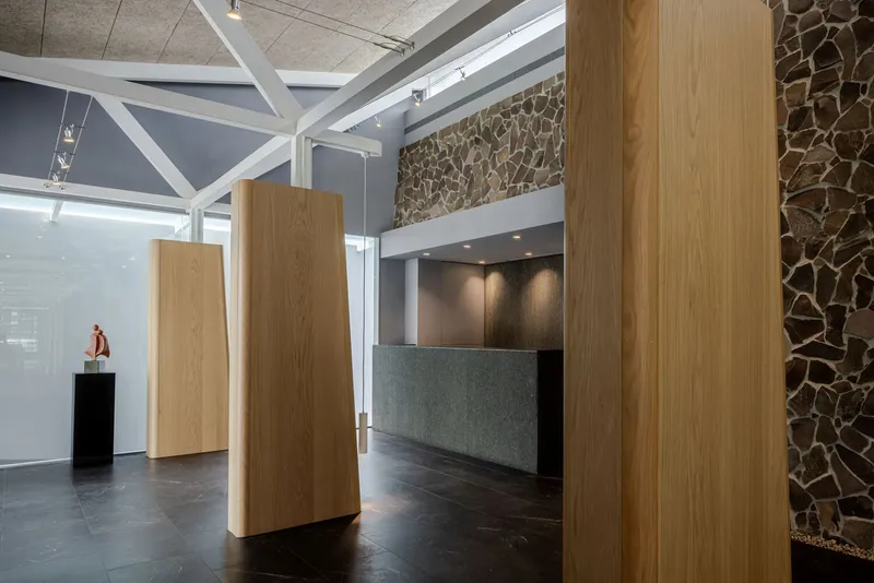 Reception desk with dark tile base and timber columns near sculptural figure on plinth