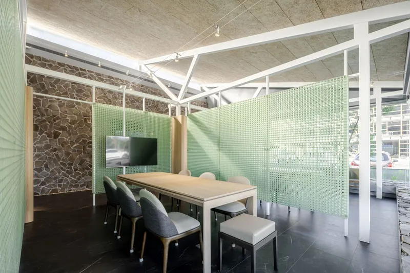 Meeting room enclosed by translucent green glass panels and white structural frame overhead