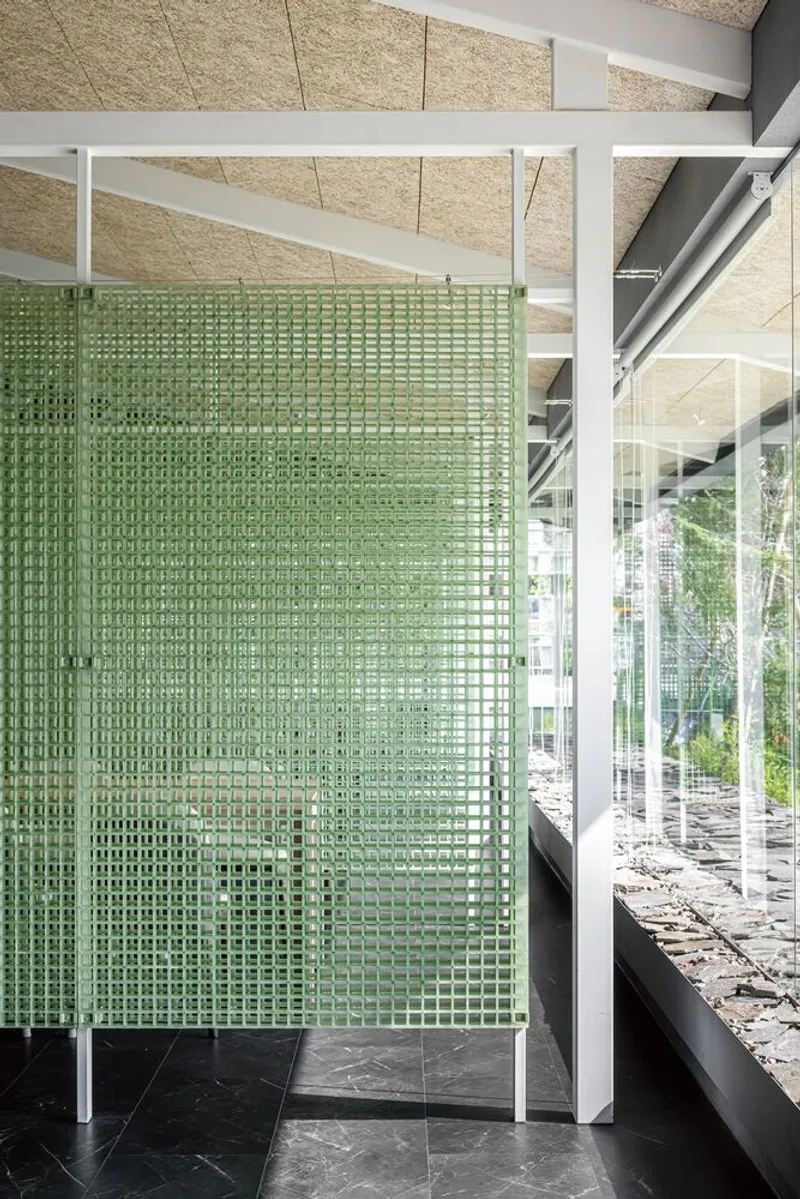 Translucent green glass block partition framed in white steel beneath a paneled particleboard ceiling