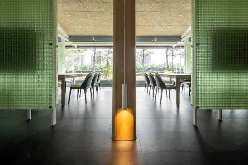 Dining area framed by green glass block panels with timber column and view to planted exterior