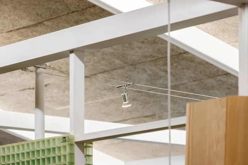 Cable lighting system suspended from white steel beams under a textured particleboard ceiling