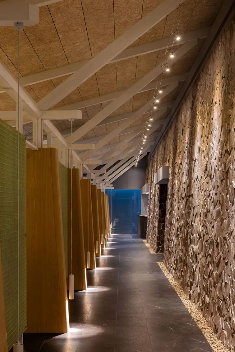 Interior corridor with textured stone wall, timber columns, exposed white trusses and string lighting overhead