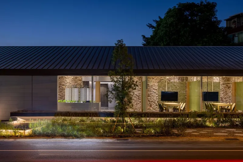 Street view at dusk showing the metal standing seam roof and illuminated stone wall facade