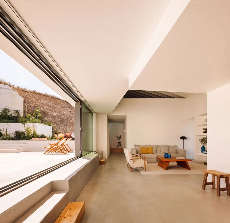 Living room with floor-to-ceiling sliding glass doors opening to a terraced courtyard with dry hillside beyond