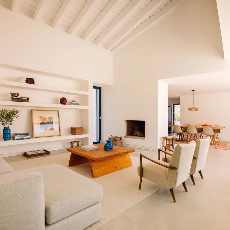 Open living space with exposed timber ceiling beams and built-in shelving flanking a recessed fireplace
