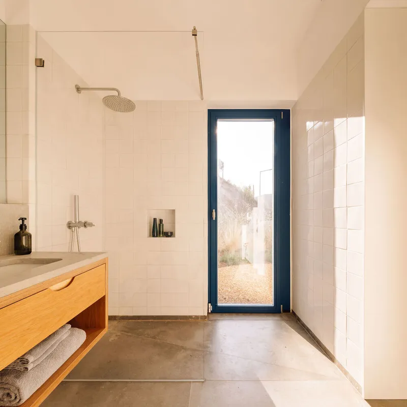 Bathroom with white square tile walls, timber vanity, and dark-framed glazed door to exterior