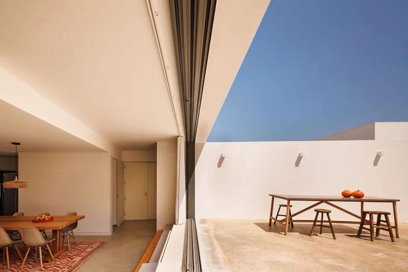 Covered terrace with fully retractable glass wall connecting interior dining area to exterior courtyard under blue sky