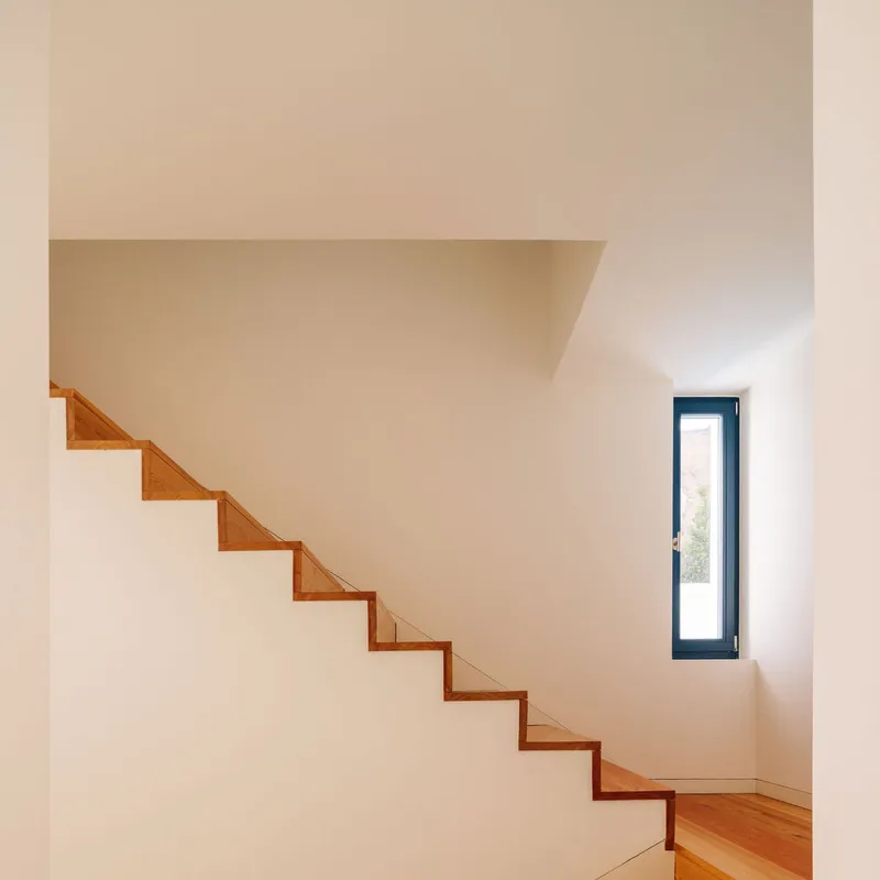 Timber floating staircase ascending white walls with a tall narrow window casting afternoon light