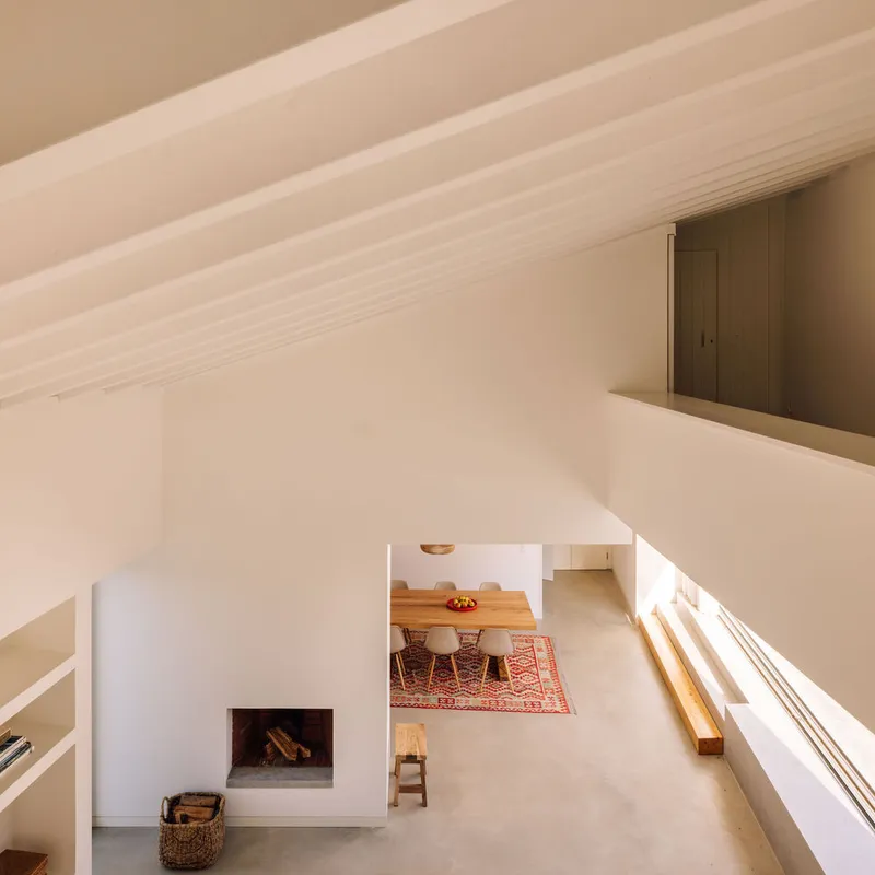 View down into double-height living space with fireplace, timber dining table and slatted sunlight