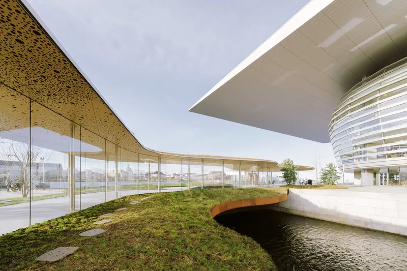 Paired cantilevered roof canopies with perforated soffits sheltering a curved glass wall and planted slope