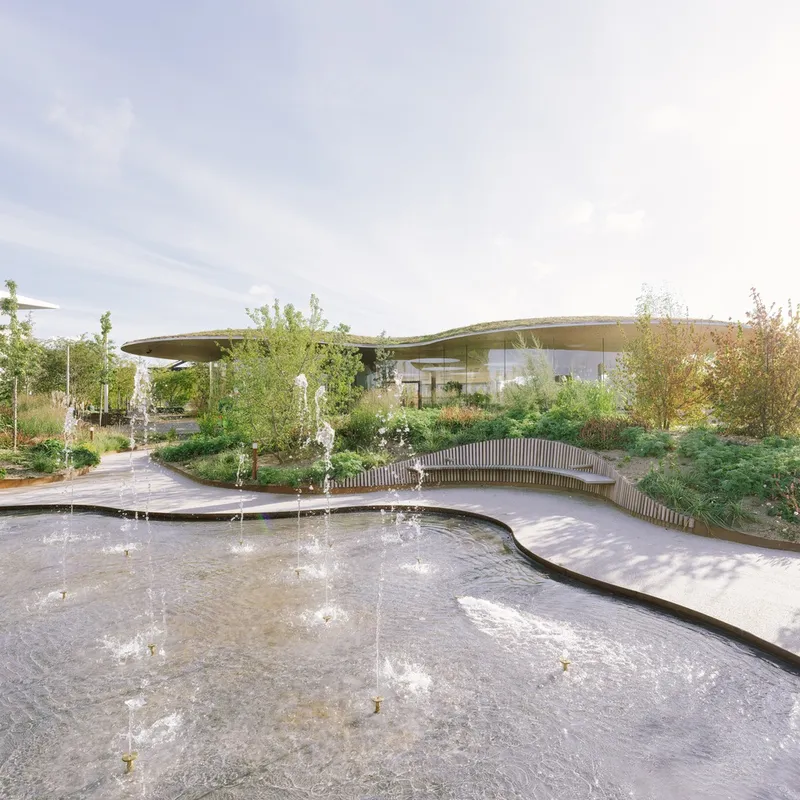 Curving water feature with vertical wood seating bench and planted slope beyond the pavilion