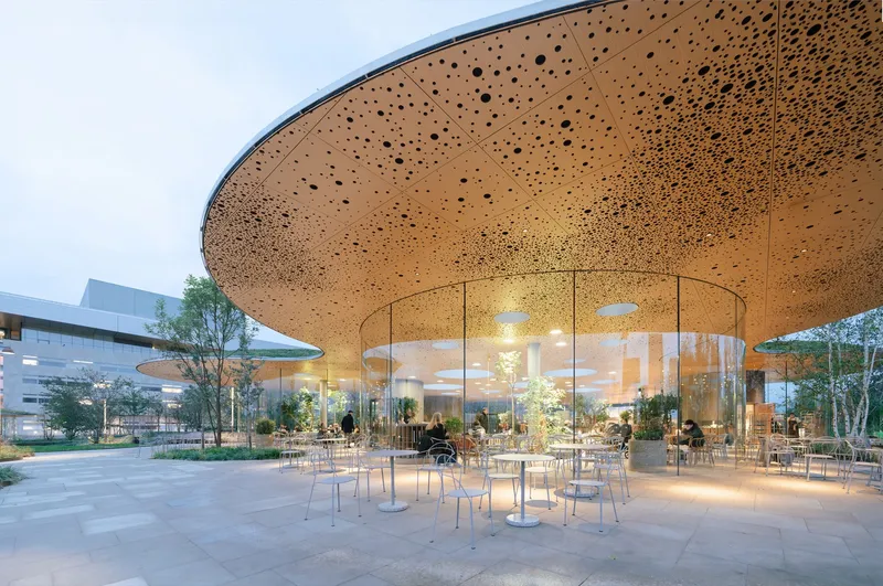 Perforated circular canopy over outdoor seating area with glazed enclosure at dusk
