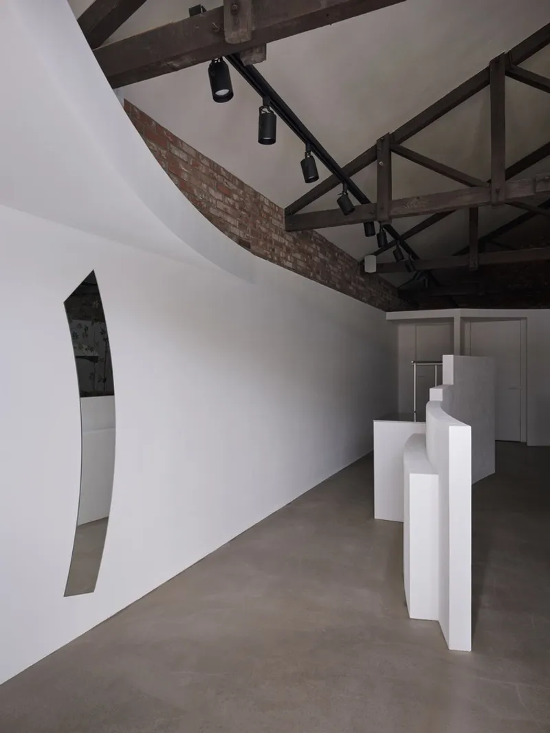 Curved white partition wall with angular cutout beneath exposed timber beams and black track lighting