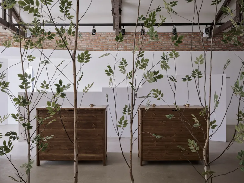 Suspended young trees in planters behind timber cabinetry with exposed brick wall beyond