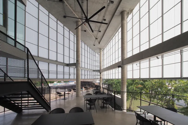 Double-height atrium with gridded translucent facade, exposed concrete ceiling and metal staircase overlooking courtyard greenery