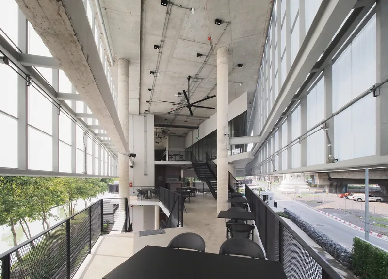 Interior mezzanine with concrete columns, ceiling-mounted fans and translucent wall panels filtering daylight