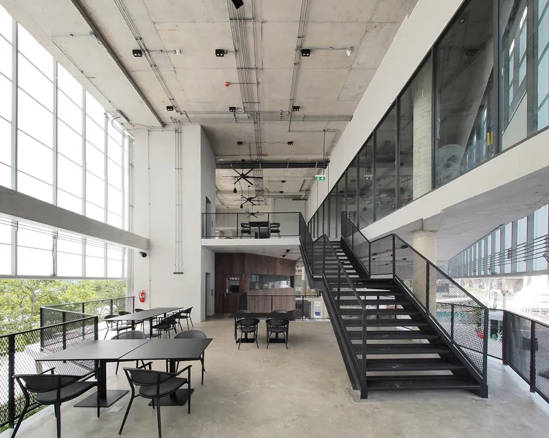 Double-height dining space with open-tread metal staircase, exposed concrete ceiling and gridded window wall