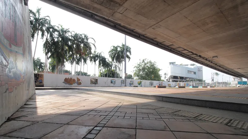 Covered plaza with exposed concrete ceiling and patterned pavement under palm trees