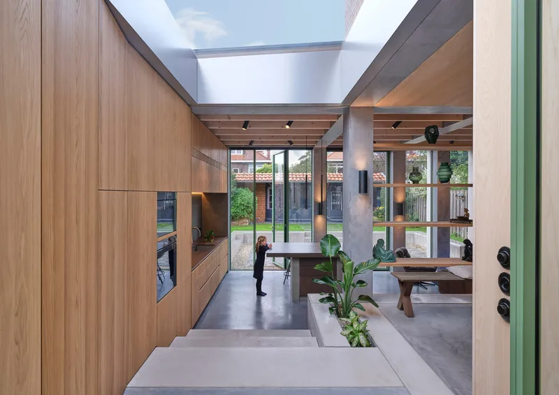 Open-plan living space with timber ceiling beams and glazed doors overlooking planted courtyard