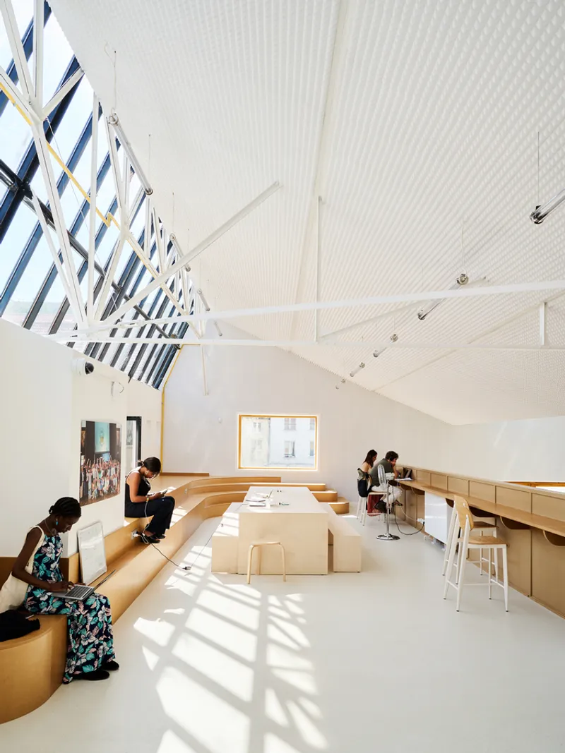 Vaulted reading room with continuous built-in timber seating and skylights casting angular shadows