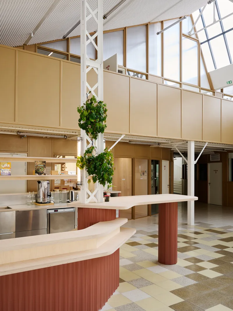 Communal kitchen with curved countertops, ribbed columns, and a climbing plant beside white steel trusses
