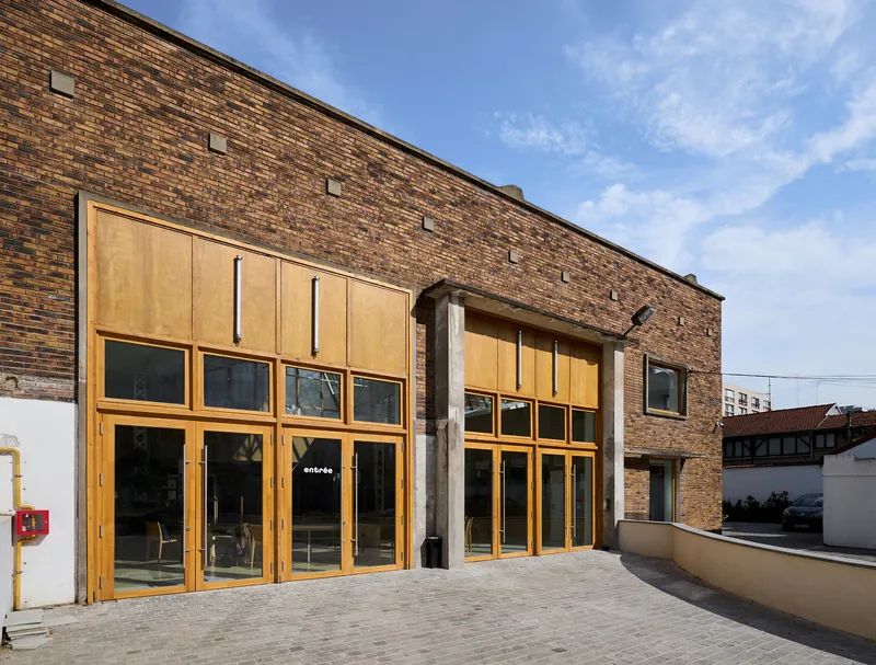 Entrance facade with new timber and glass infill within the original brick warehouse wall under clear sky