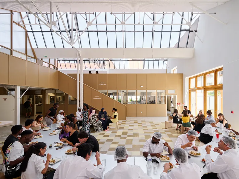 Students and volunteers seated at long tables beneath the skylight during a communal meal