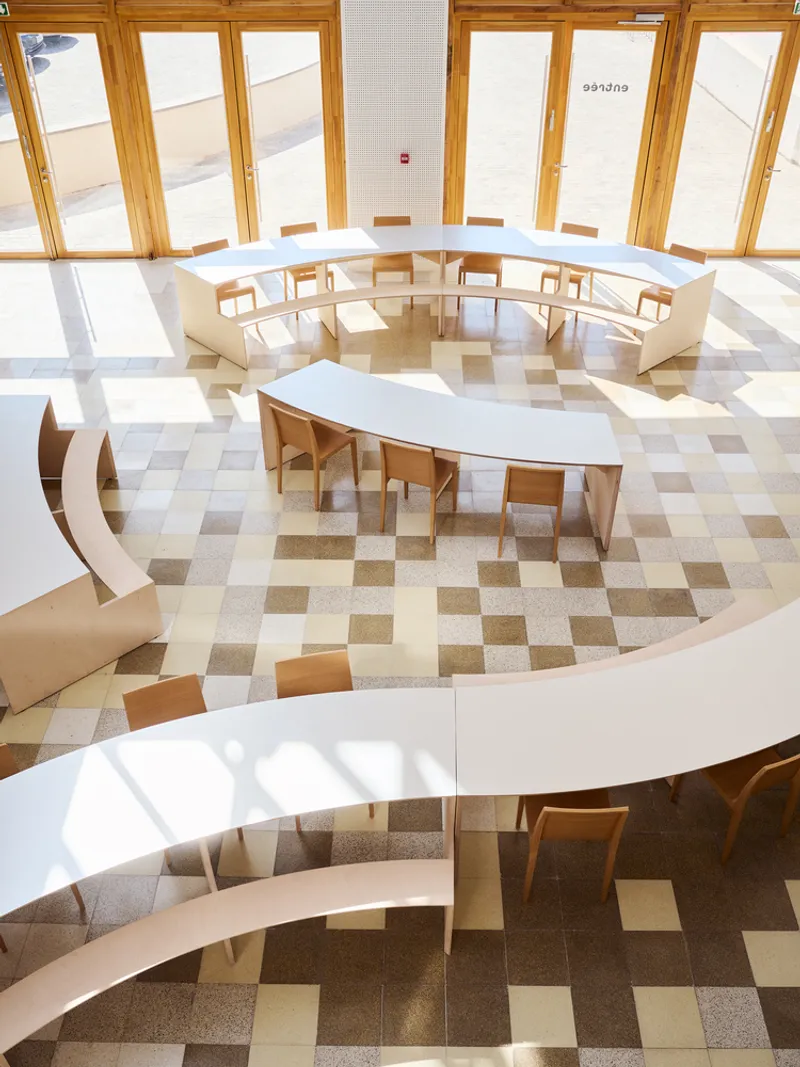 Top-down view of curved white benches and tables arranged around circular terrazzo floor pattern