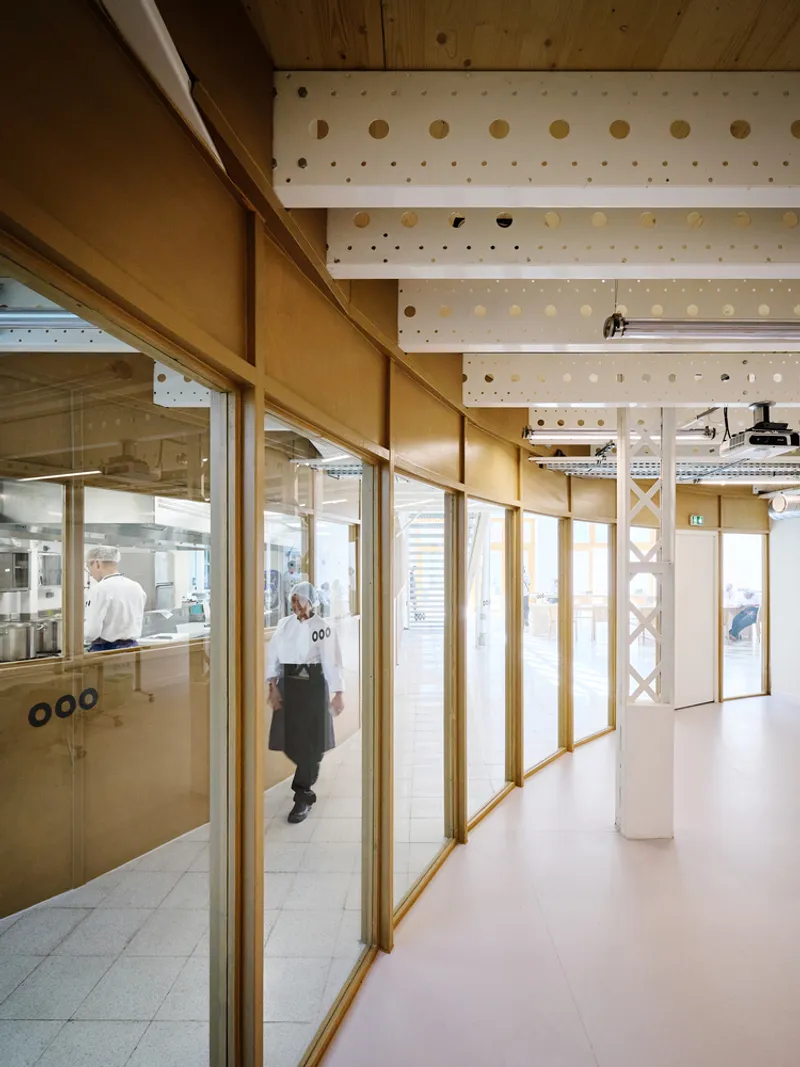 Corridor with timber-framed glazing and perforated plywood ceiling panels as a figure walks past