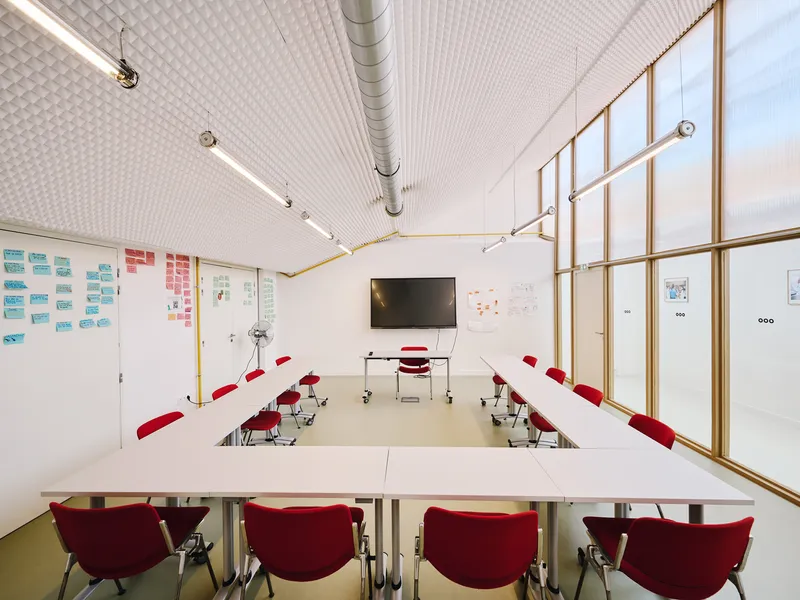 Classroom with red chairs at white tables and timber-framed frosted glass partition wall