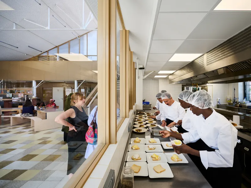 Kitchen pass-through with timber frame glazing separating the cooking zone from the checkered floor dining area